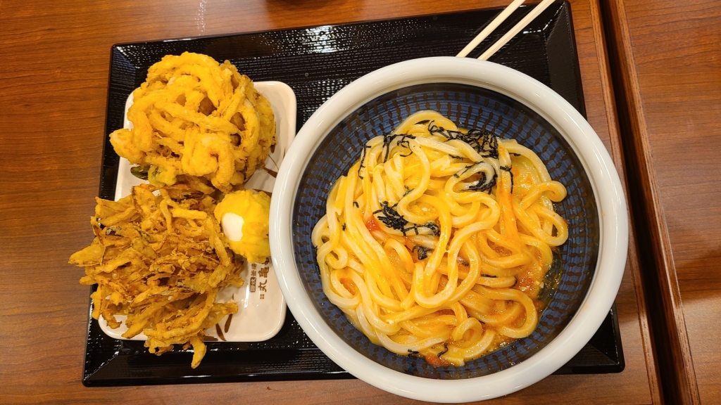 お盆に載った明太釜玉うどん・得、野菜かき揚げ、海老とほたてのかき揚げ、半熟玉子天の写真